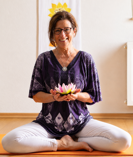 Frau sitzt auf Yogamatte und lächelt in die Kamera