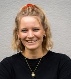 Frau mit blonden Haaren, schwarzem T-Shirt und Goldkettchen lacht in die Kamera