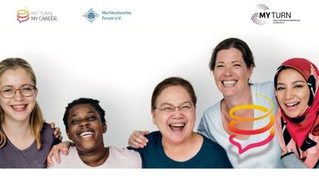 Fünf Frauen lächeln nebeneinander in die Kamera. Sie stehen eng und haben ihre Hände auf Schultern einer jeweils anderen Frau gelegt.