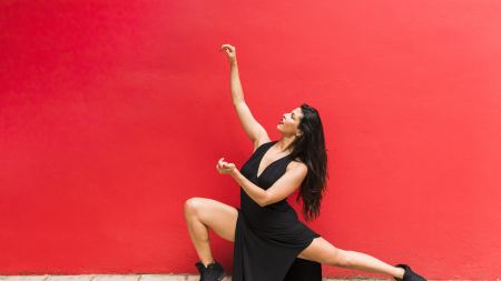 Frau in schwarzem Kleid in hockender Tanzposition vor roter Wand
