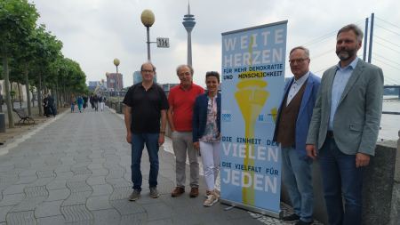 Fünf Personen stehen rund um einen Banner am Rheinufer
