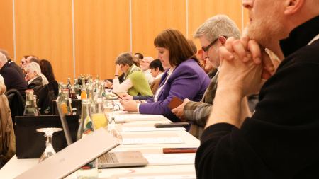 10 Gäste aus dem Publikum sitzen nebeneinander in einer Tischreihe