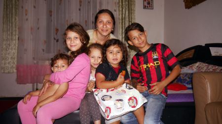 Dunkelblonde Frau sitzt mit fünf Kindern im Alter von 2 bis 8 auf einem Bett