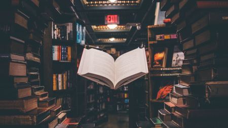 Aufgeschlagenes Buch schwebt in Bibliothek zwischen Regalen
