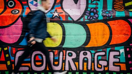 Person läuft an bunter Grafitti-Wand mit Schriftzug "Courage" vorbei