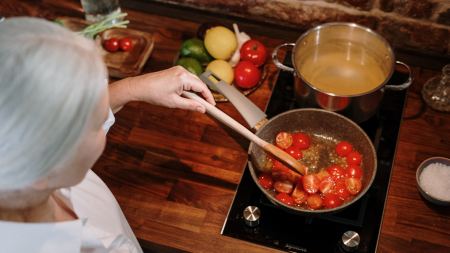 Grauhaarige Person steht am Herd und kocht mit Tomaten