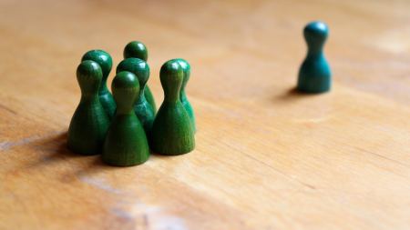 eine Gruppe grüner Spielfiguren grenzt eine blaue Spielfigur aus