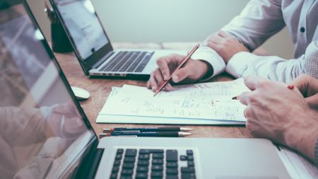 Person arbeitet mit Stift und Zettel vor einem Laptop