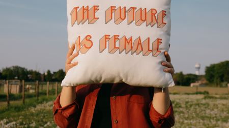 Frau hält sich Kissen mit der Aufschrift "The Future is Female" vor das Gesicht