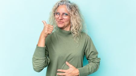 Frau hält sich den Bauch und zeigt zufrieden den Daumen hoch