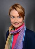 Portrait von Anna Wiebke Klie (Frau mit Kurzhaarfrisur, buntem Schal, pinkem Oberteil und Blazer lächelt in die Kamera)